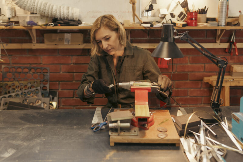 Artist working on a piece at a workshop, using tools and equipment on a workbench.