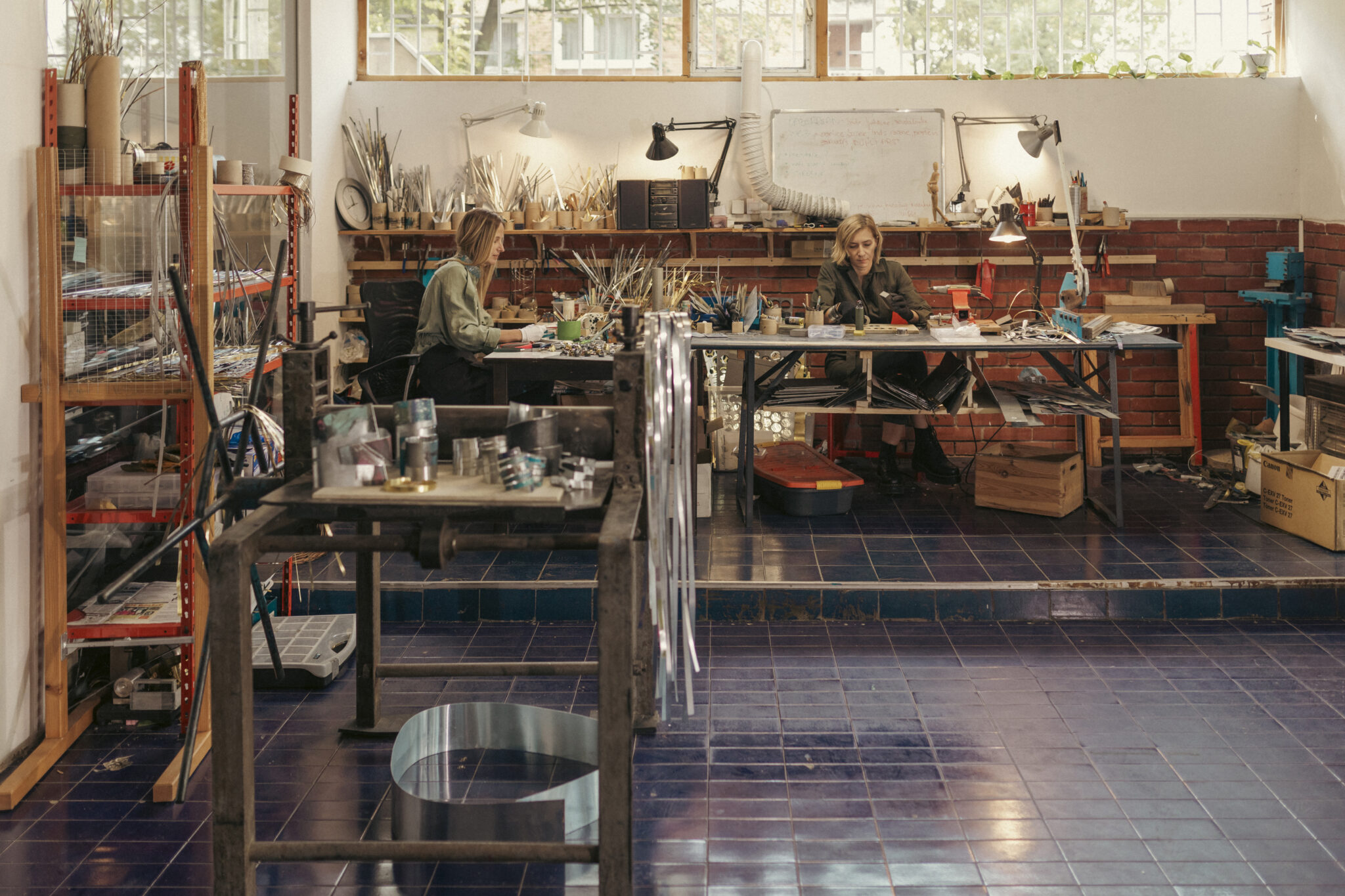 Nuhić and Šarić working in a studio filled with tools and materials, surrounded by tables and shelves.