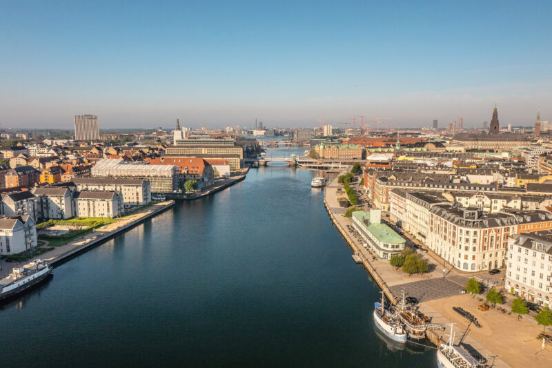 Aerial view of Copenhagen's harbour, showcasing buildings, boats, and a clear blue sky.