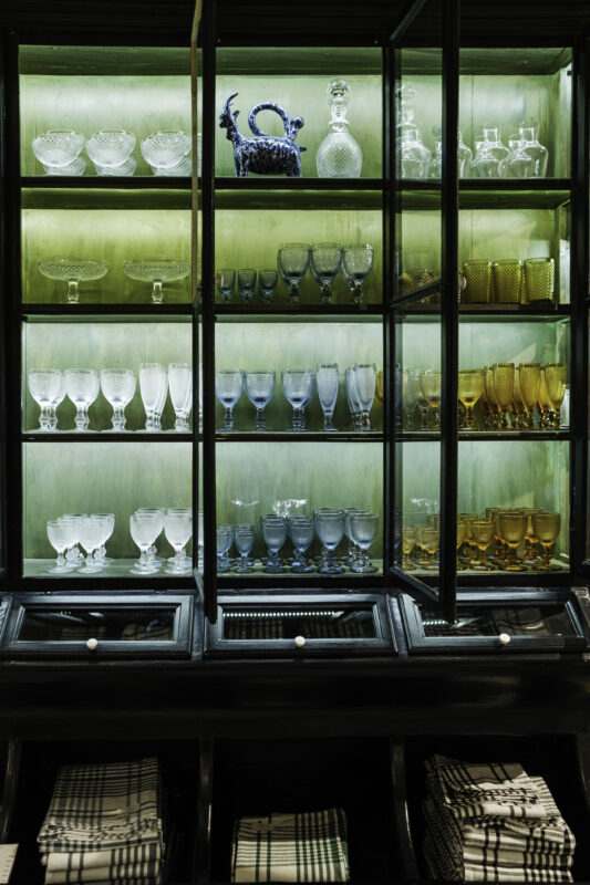 Glassware display in a cabinet featuring various crystal and colored glasses, illuminated with green light.