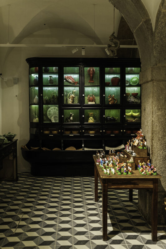 Display of colorful Portuguese antiques and crafts in a shop, featuring a black cabinet and a wooden table with figurines.