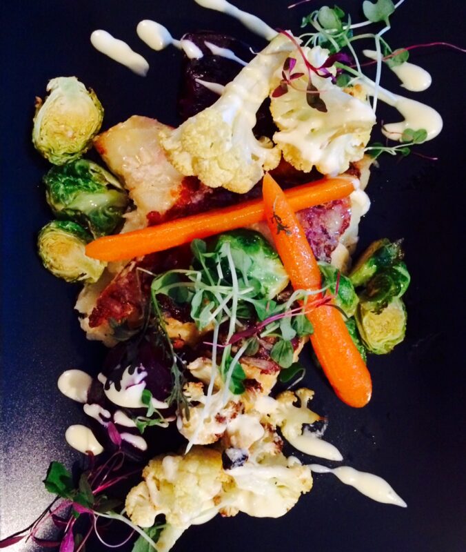 Colorful plate featuring roasted vegetables like Brussels sprouts, carrots, and cauliflower drizzled with sauce, served at...