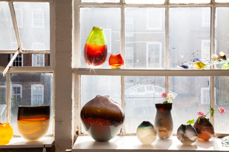 Colorful glass vases and sculptures displayed on a windowsill, illuminated by natural light at Cockpit Studios, London.