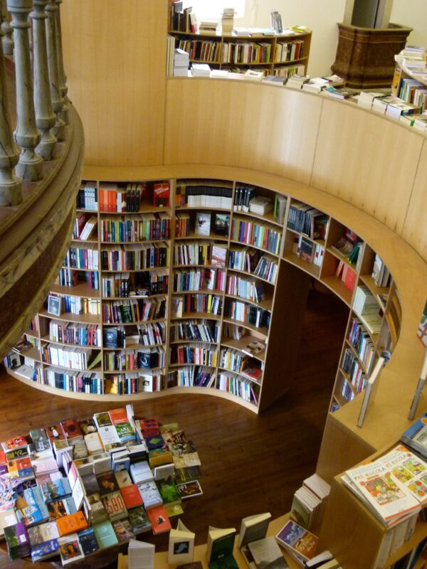 Curved wooden bookshelves filled with colorful books in a spacious bookstore, with a wooden railing visible above.