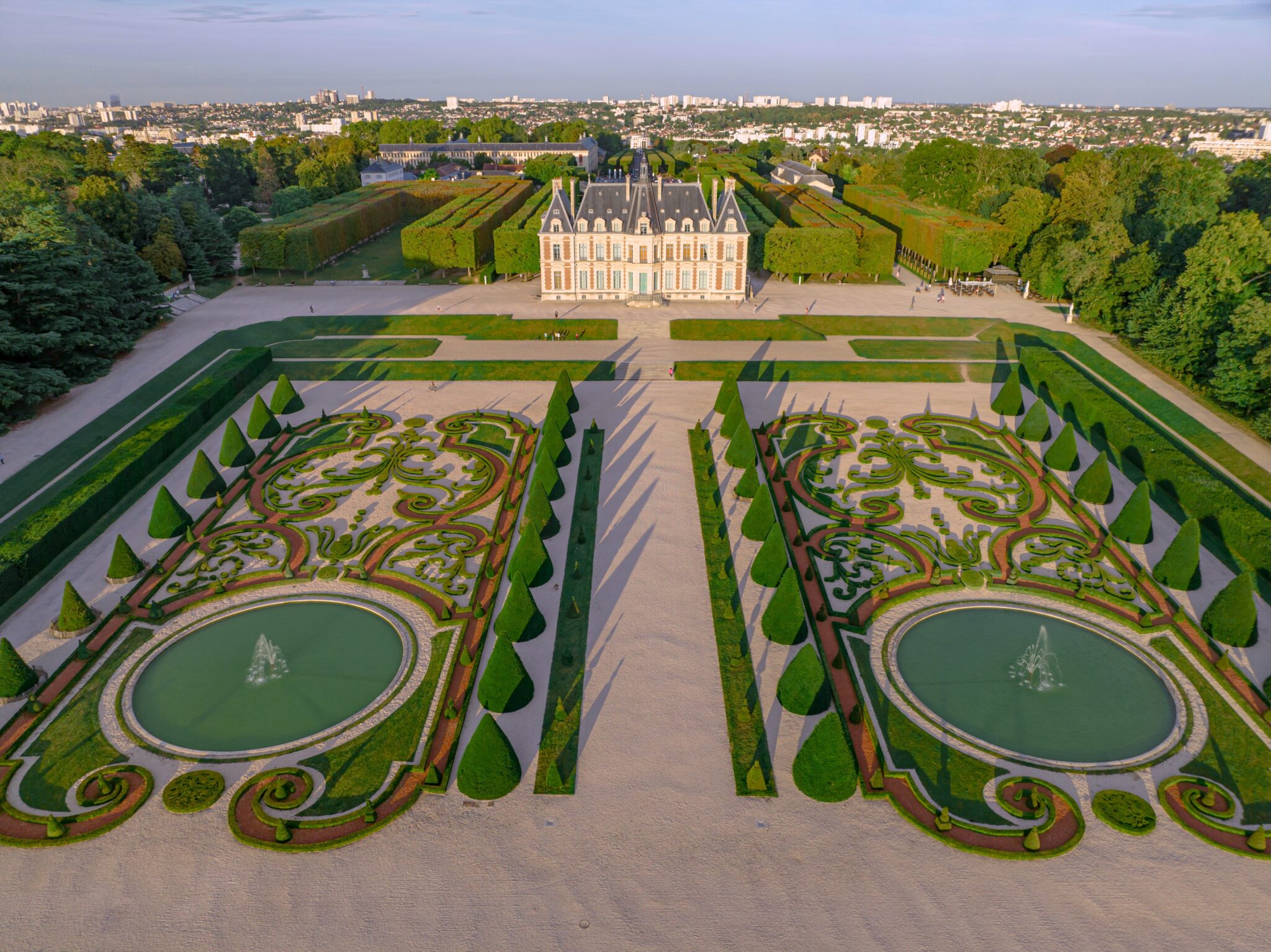 Aerial view of Parc de Sceaux, featuring manicured gardens, fountains, and a grand chateau in the background.