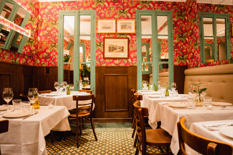 Cozy dining area in Murillo Café with floral wallpaper, wooden furniture, and neatly set tables.
