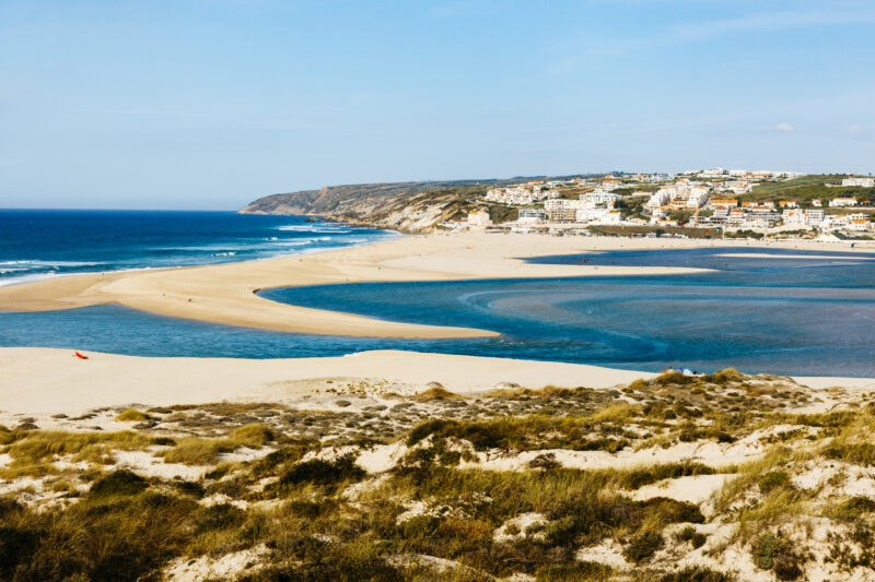 Praia do Bom Sucesso in Óbidos, featuring sandy beaches, blue waters, and a coastal town in the background.