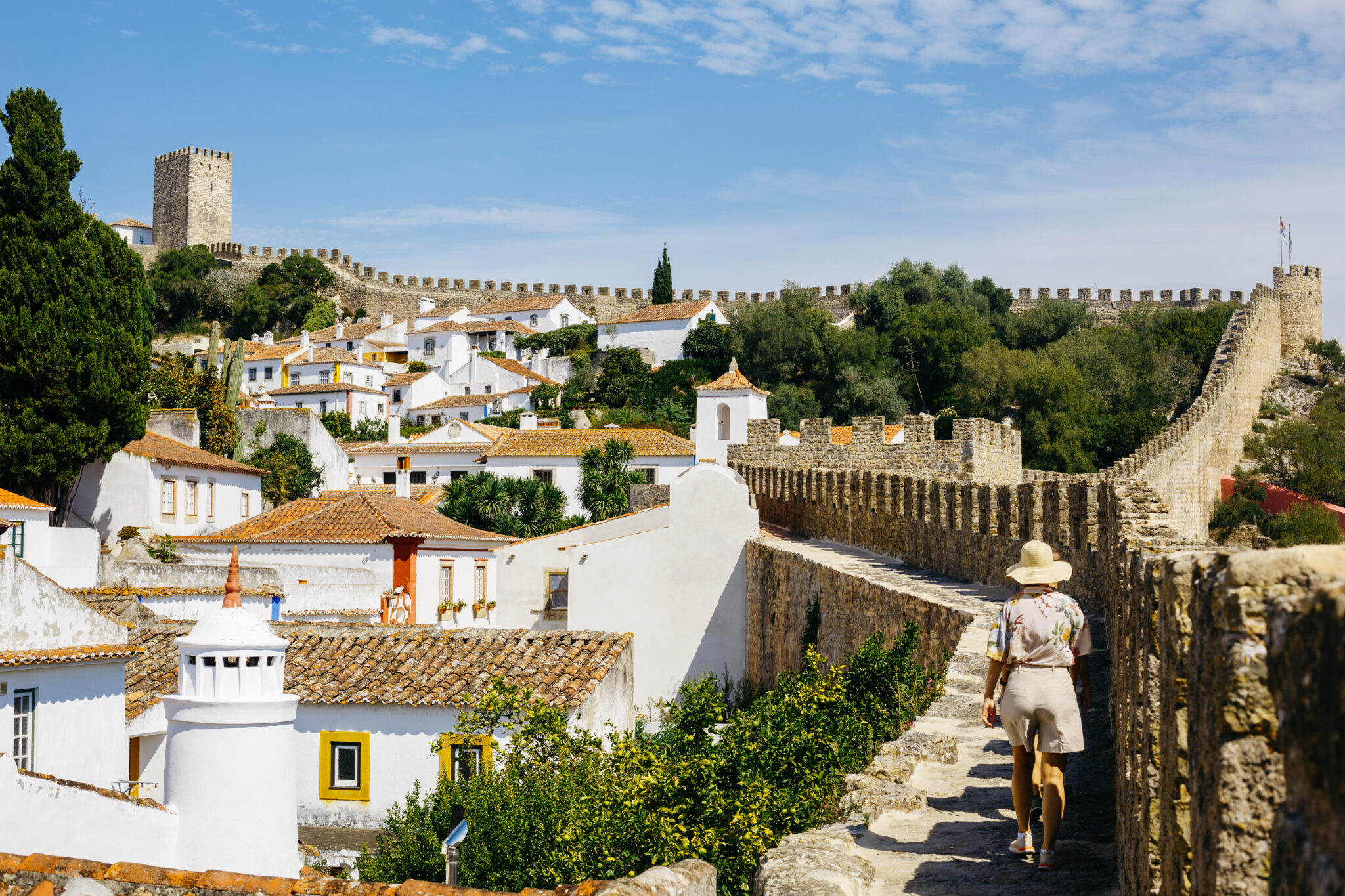 Scenic view of Vila de Óbidos with medieval walls, white houses, and a person walking along the stone path.