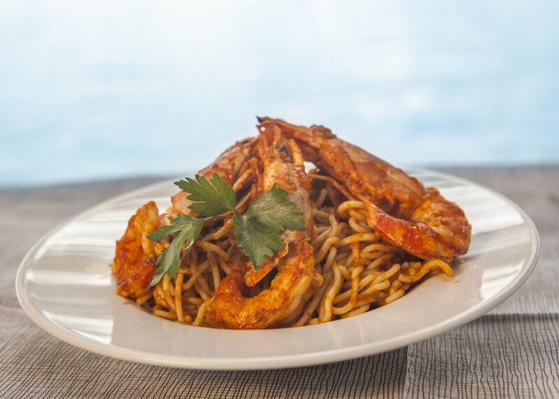 Shrimp pasta garnished with parsley on a white plate, set against a light blue background.