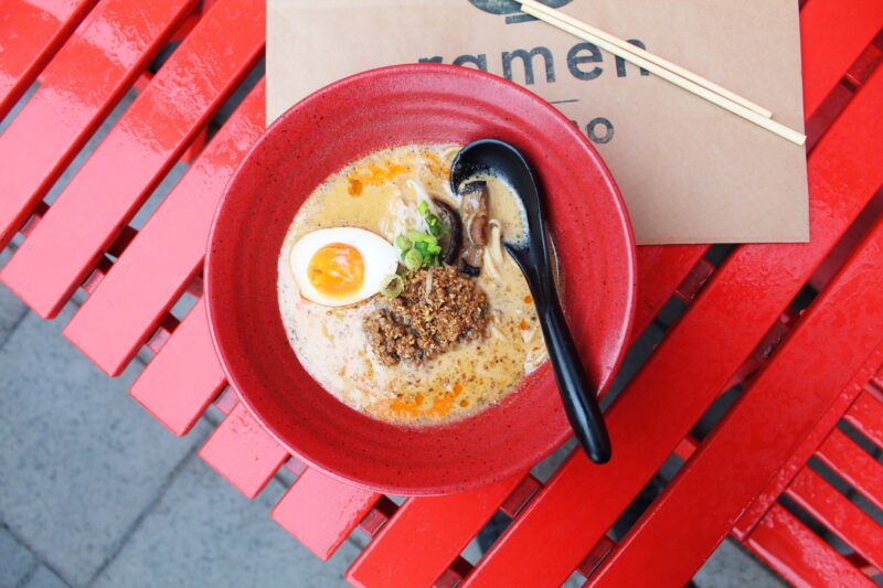 Bowl of Tantanmen ramen with egg, green onions, and ground meat on a red table at Momo.