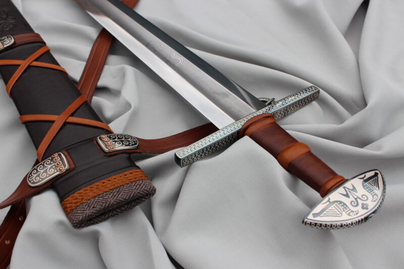 Decorative sword with a detailed hilt and scabbard, resting on a light gray fabric background.