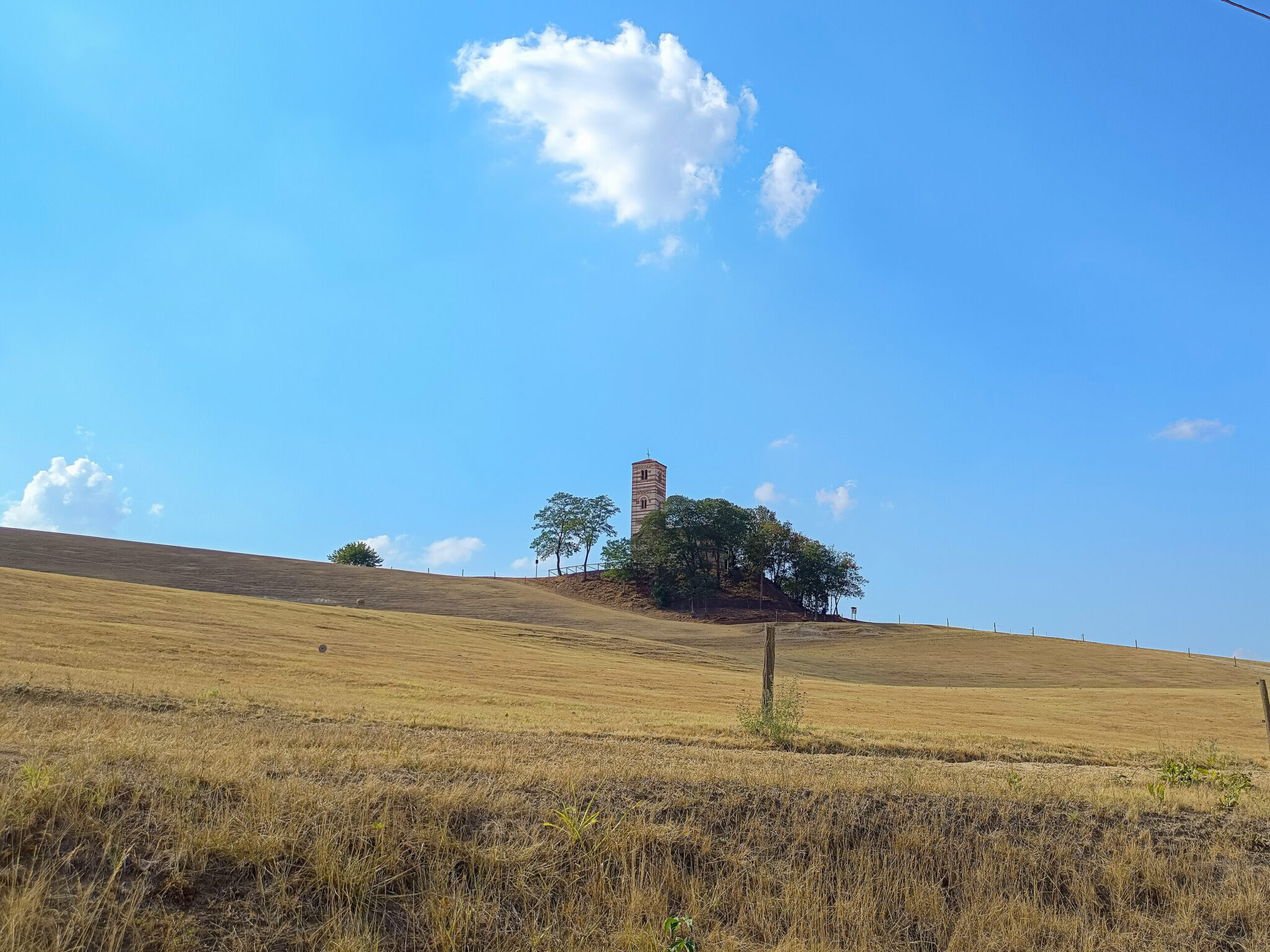 Rolling golden hills under a blue sky with a solitary tower and trees in the distance.