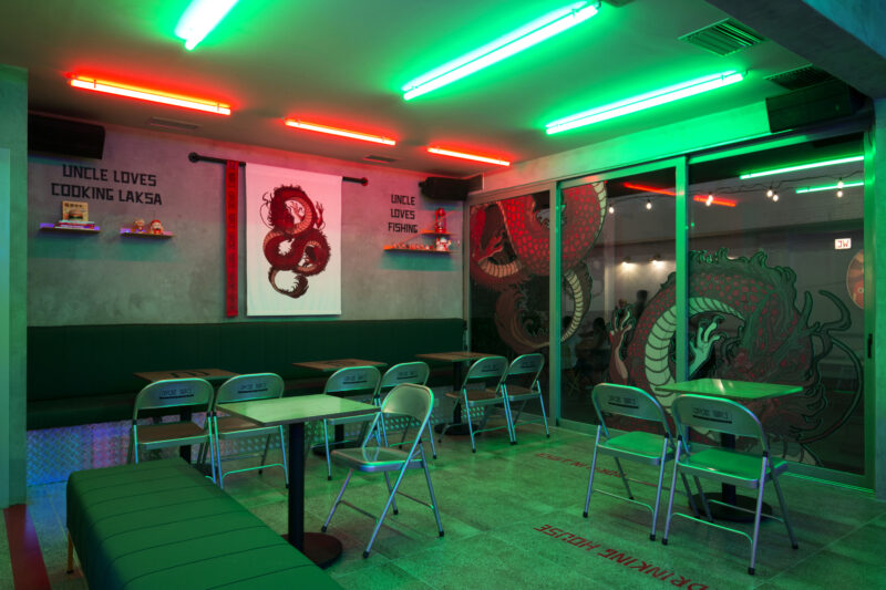 Interior of Uncle Tan's Drinking House featuring neon lights, green seating, and dragon murals on the walls.