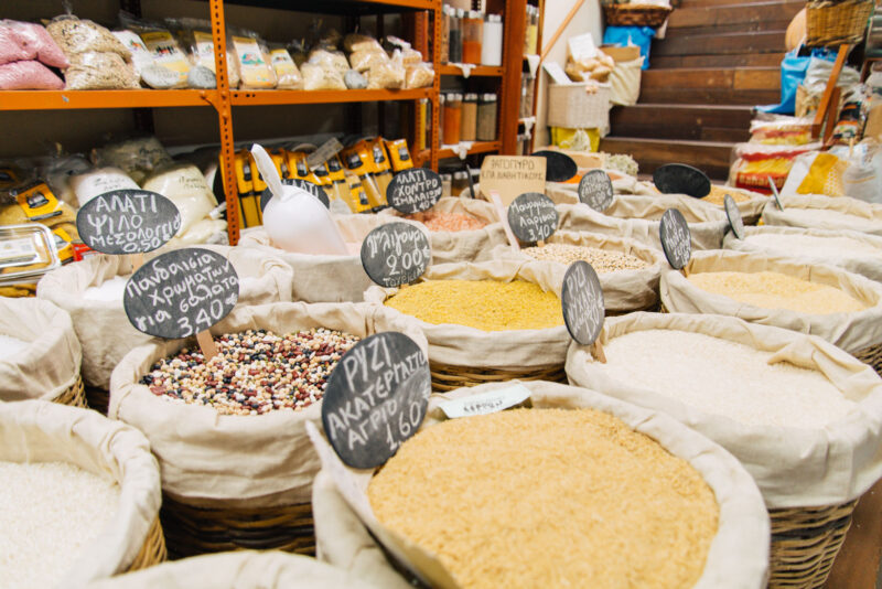 Bags of various grains and legumes in a market, labeled with prices on small chalkboards, showcasing local flavors.
