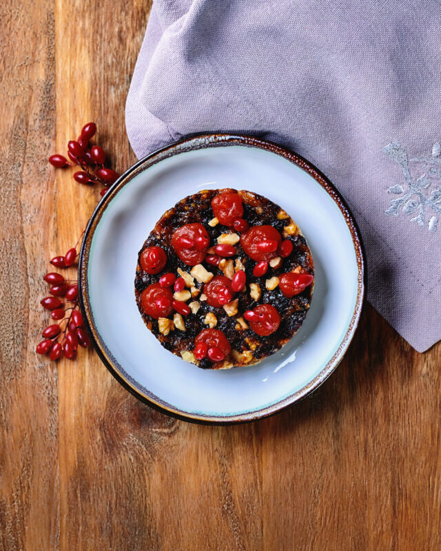 Halva topped with nuts and dried fruit, served on a white plate with a purple cloth and decorative berries.