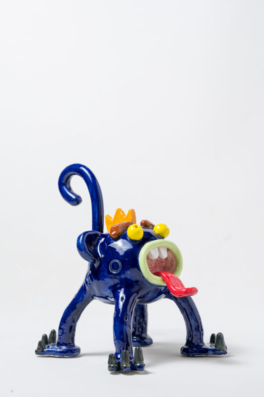 Ceramic sculpture of a blue monkey with a crown, large eyes, and a tongue sticking out, created by Carlos Manuel Gonçalves.