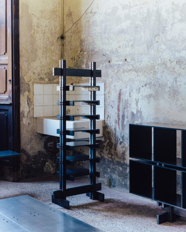 Black shelving unit against a textured wall with peeling paint, alongside a white sink and a black storage unit.