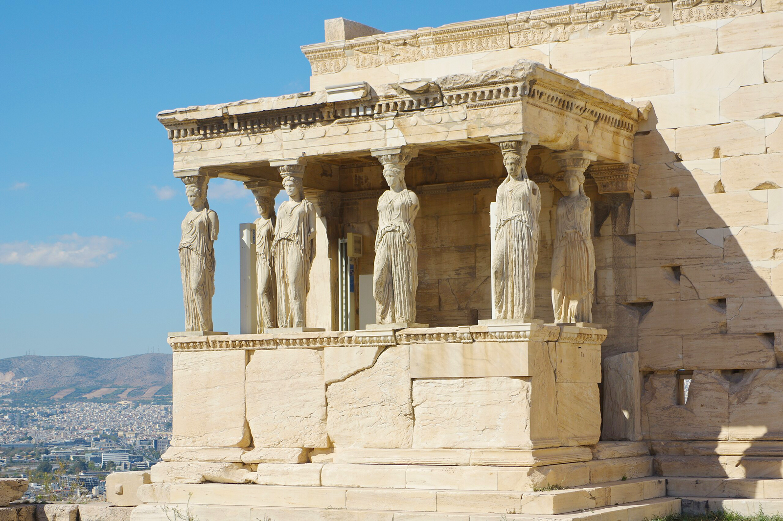 Erechtheion temple on the Acropolis, featuring Caryatids, with a view of Athens in the background.