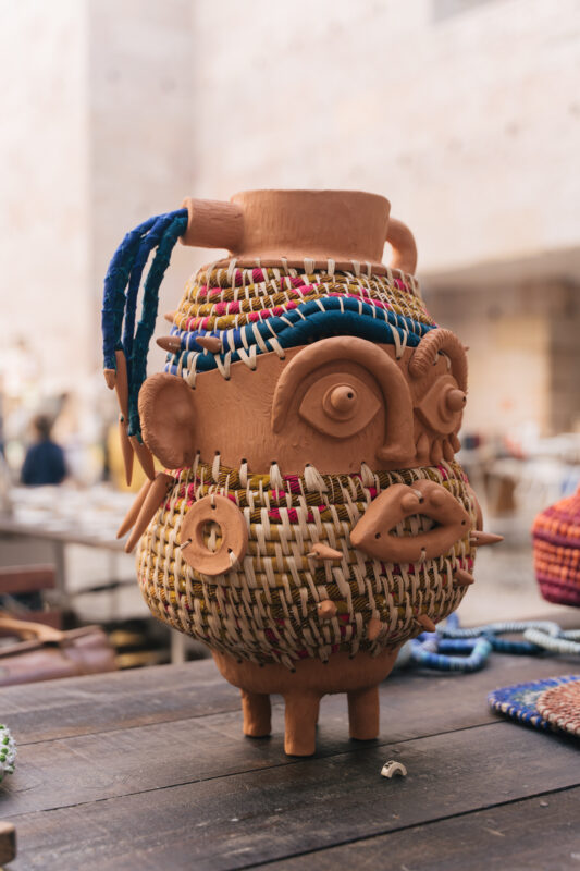 Ceramic sculpture with woven details, featuring eyes and facial features, displayed on a wooden table.
