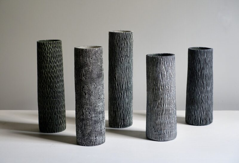 Five unique, textured ceramic vases in varying heights, displayed against a neutral background.