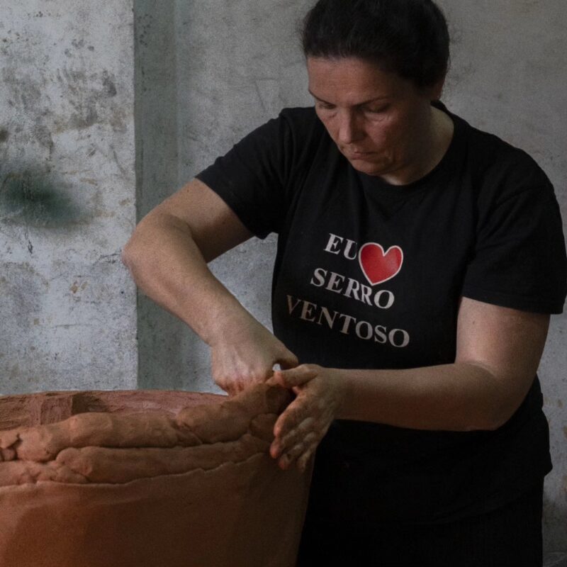 Sandra Borges shaping red clay using the slap building technique, wearing a black shirt with a heart design.