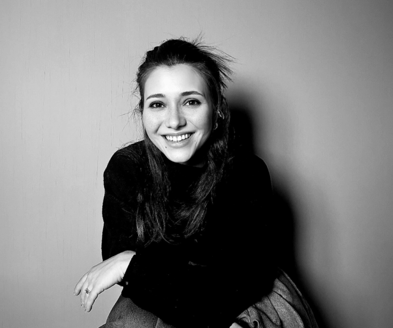 Portrait of Semiha Sera Güllü Ülgen smiling, seated against a plain background, wearing a black sweater.