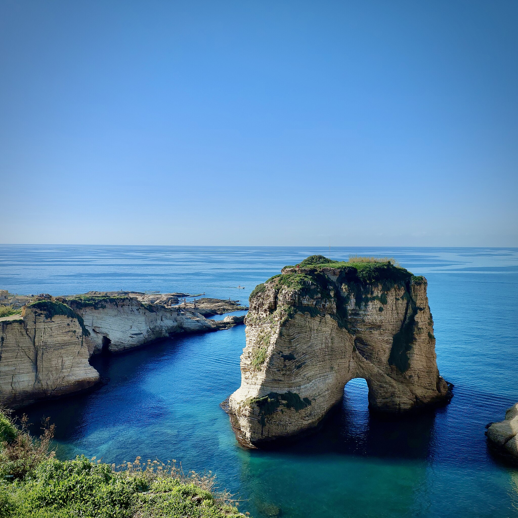 Pigeon Rock stands majestically in the Mediterranean Sea, surrounded by clear blue waters and a bright sky.