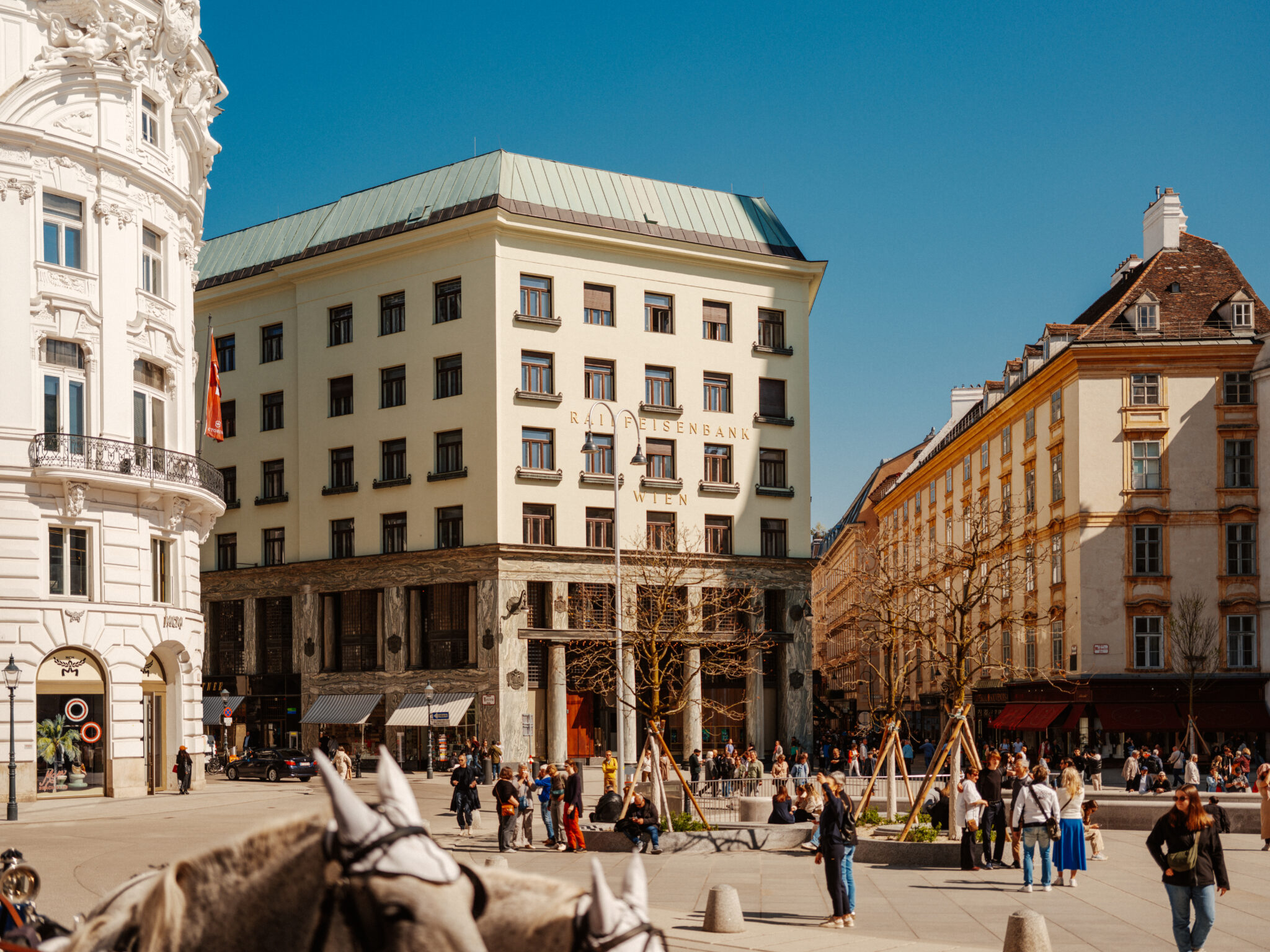 Looshaus at Michaelerplatz in Vienna, featuring people enjoying a sunny spring day amidst urban architecture.