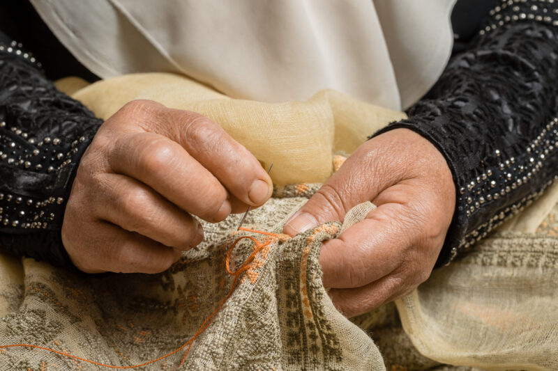 Hands of a person sewing intricate patterns on fabric, showcasing traditional craftsmanship in Beirut, Lebanon.