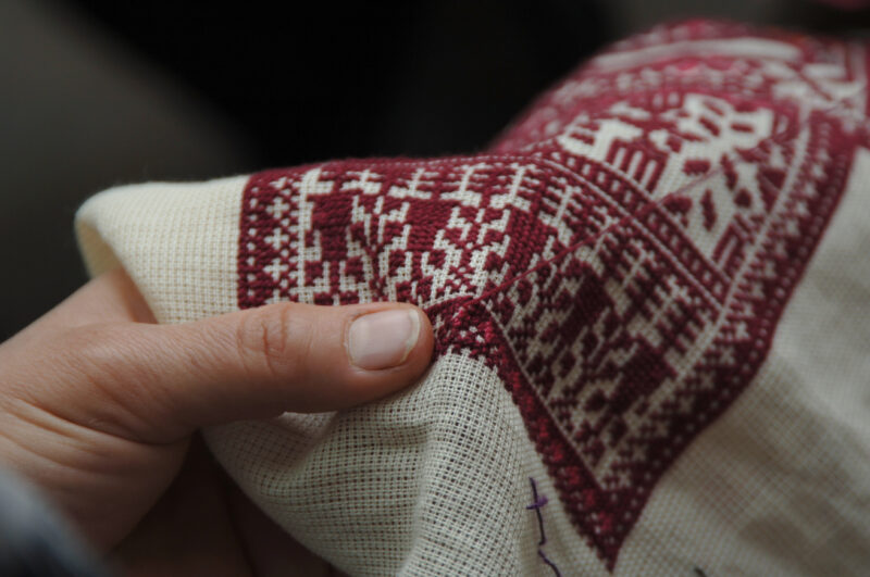 Close-up of a hand holding embroidered fabric featuring intricate red and white patterns.