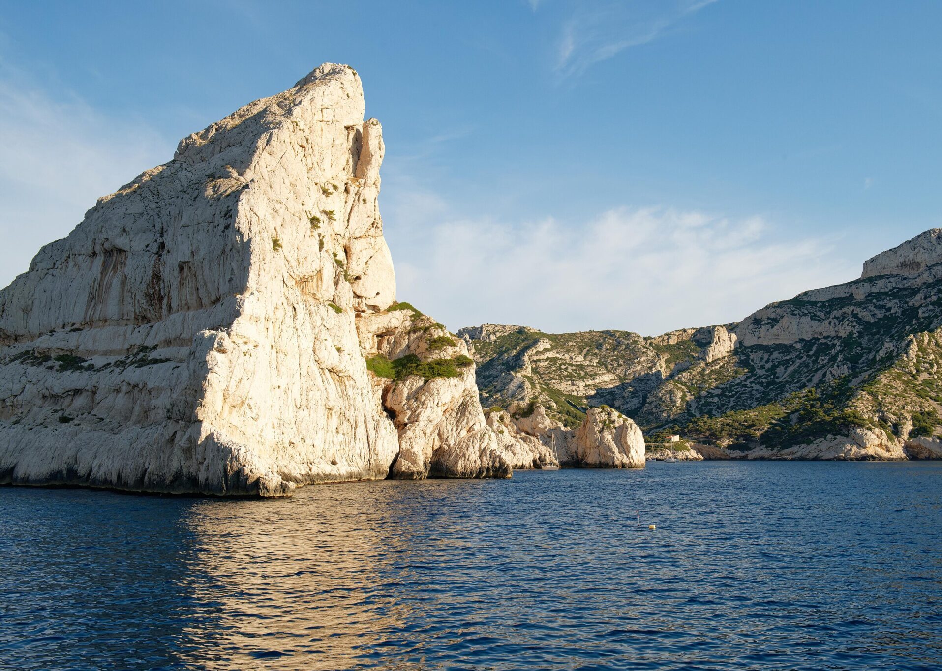Rocky cliffs rise above calm blue waters under a clear sky in the peaceful seaside of Marseille.