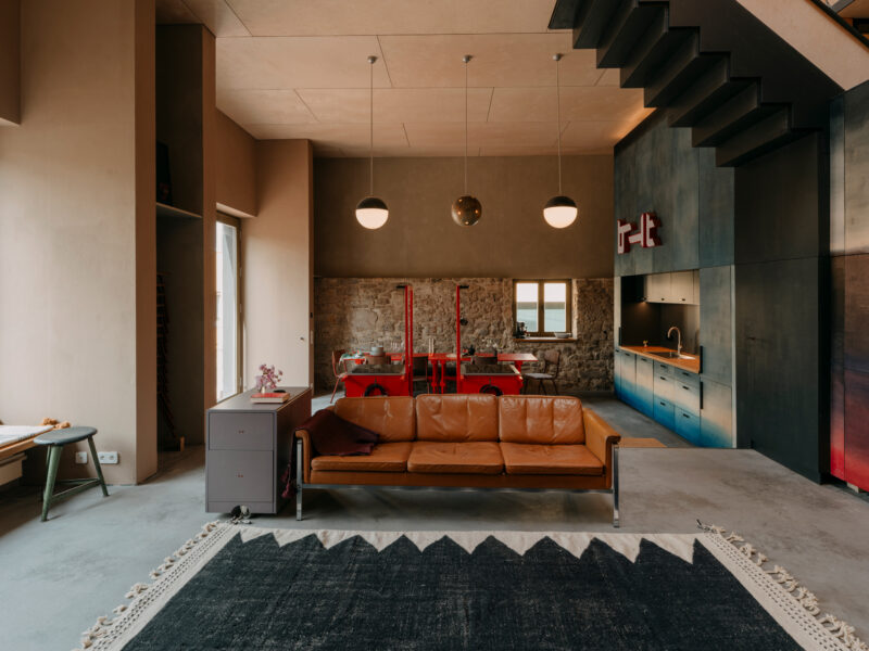 Spacious ground floor with a leather sofa, modern kitchen, and stone wall, inviting guests to linger.