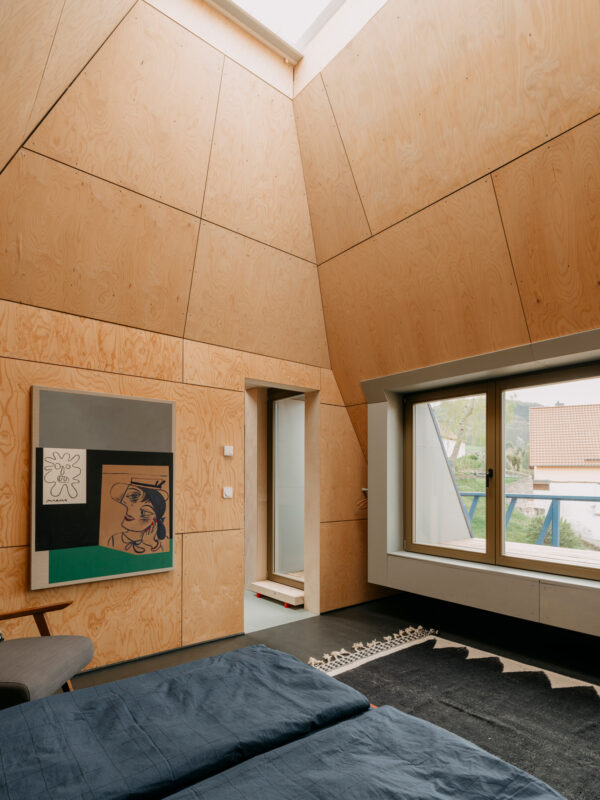 Light-filled room with wooden walls, featuring a painting, large windows, and a cozy bed.