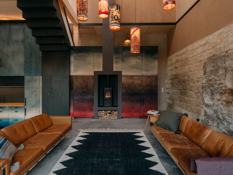 Modern living room featuring two brown leather sofas, a black patterned rug, and artistic pendant lights above a central f...