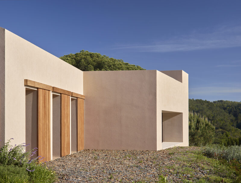 Modern architectural structure with wooden accents, surrounded by greenery under a clear blue sky.