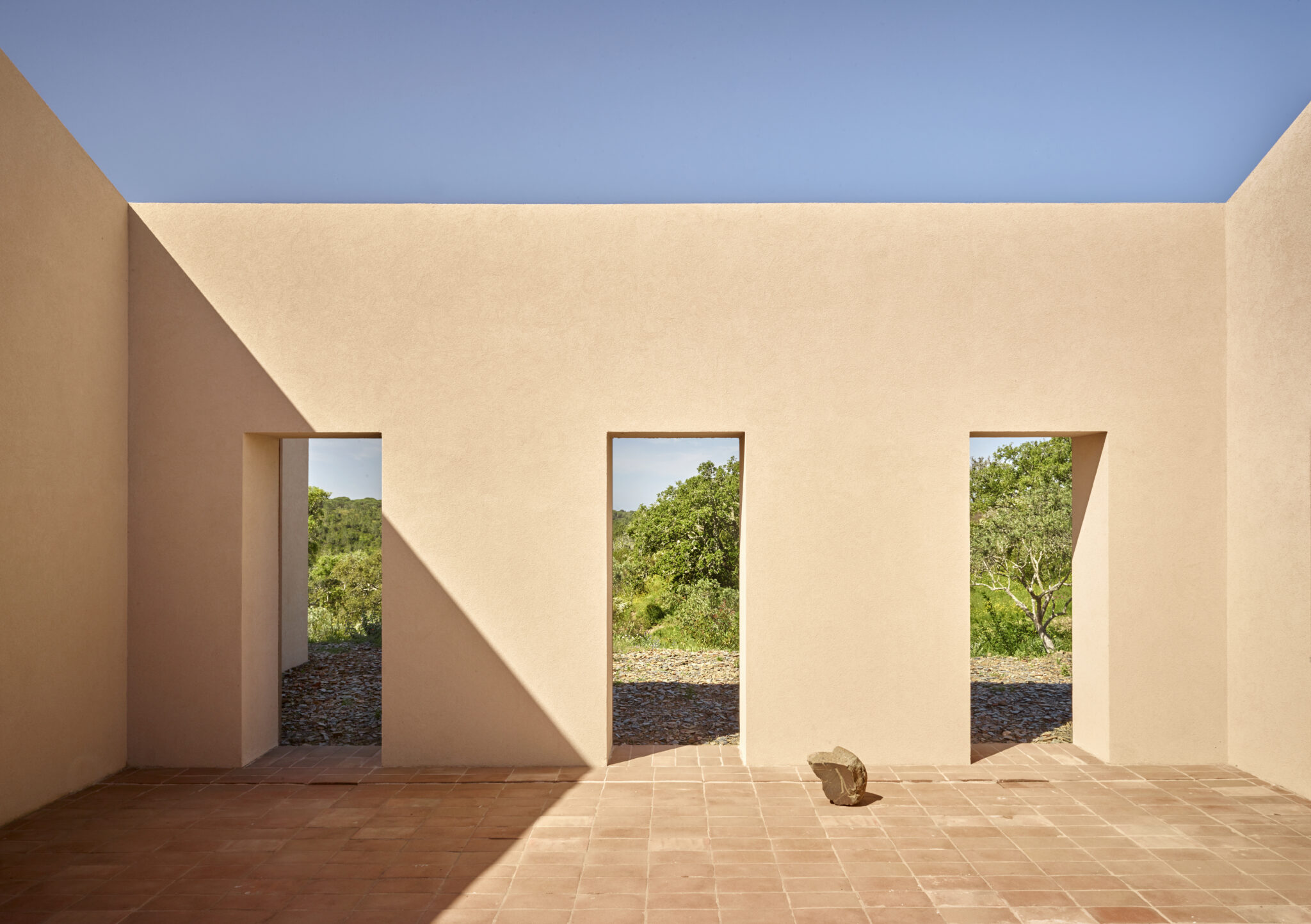 Interior of a minimalist structure with three doorways, natural light casting shadows on a textured wall.