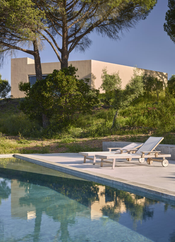 Modern villa with a pool, sun loungers, and surrounding greenery under a clear blue sky.