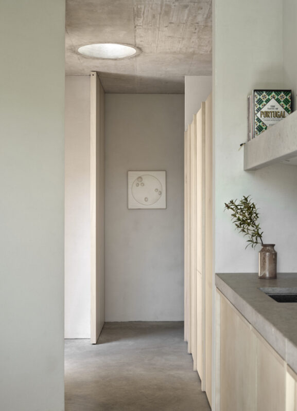 Minimalist kitchen corridor with light-colored cabinetry, a circular skylight, and a framed artwork on the wall.