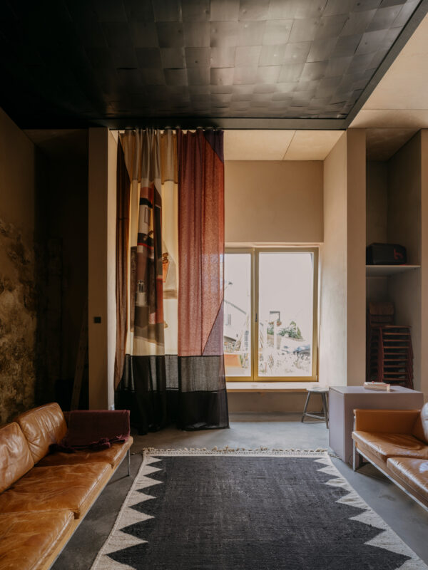 Curtains in warm tones of fire and ashes hang in a modern room with a leather sofa and large window.
