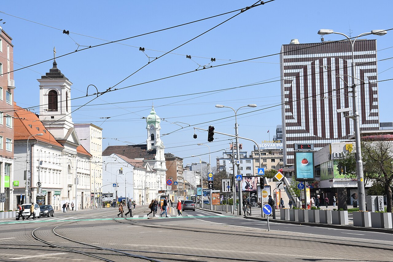 Bratislava city center featuring a mix of historic and modern architecture, with tram lines and pedestrians.