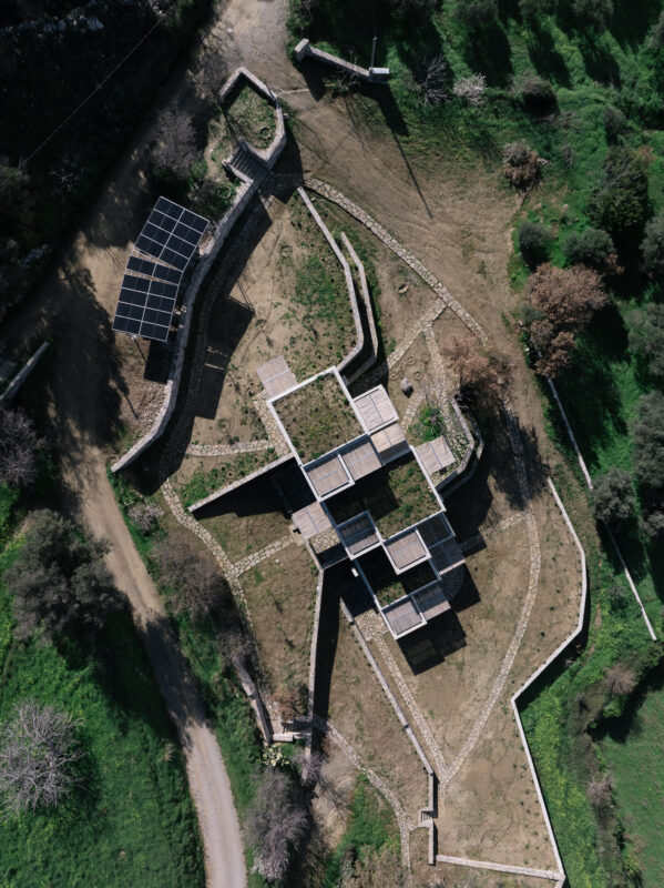 Aerial view of hand-built walls following the land's contours, surrounded by greenery and solar panels.
