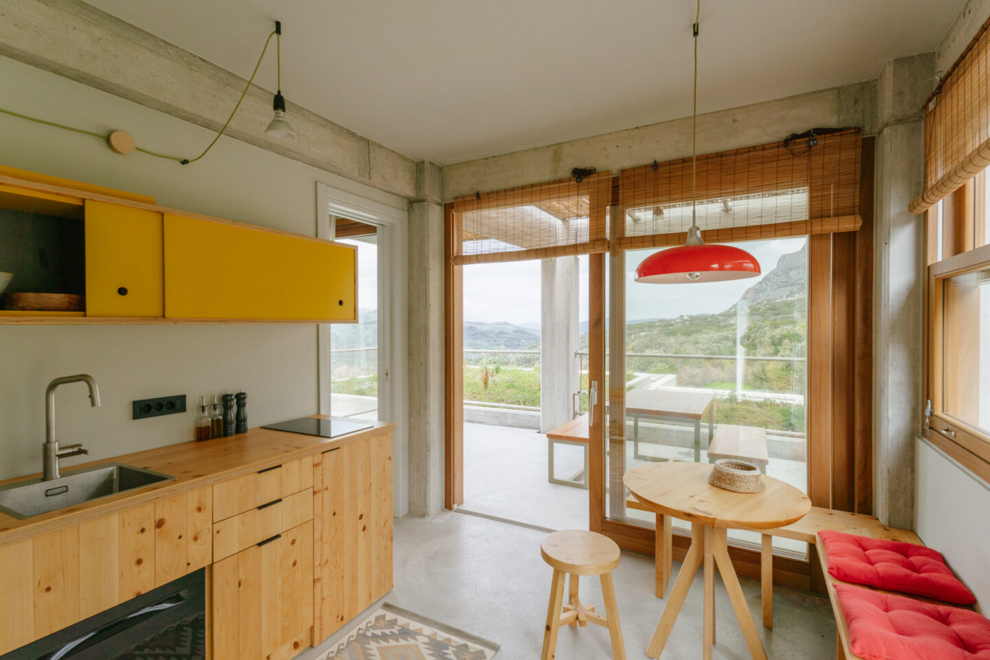 Minimalist kitchen with wooden cabinetry, yellow accents, and a view of nature through large windows.