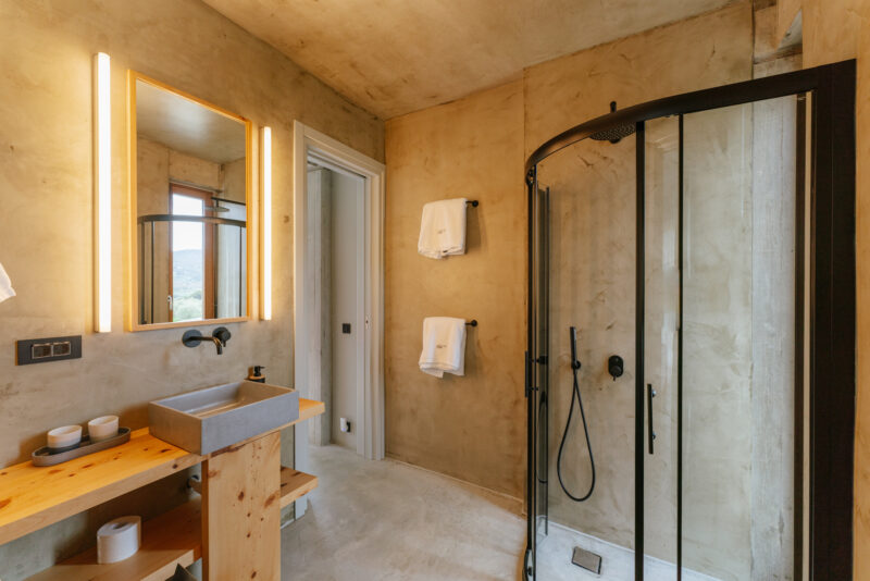 Modern bathroom featuring a concrete wall, wooden vanity, and a glass shower with warm lighting.