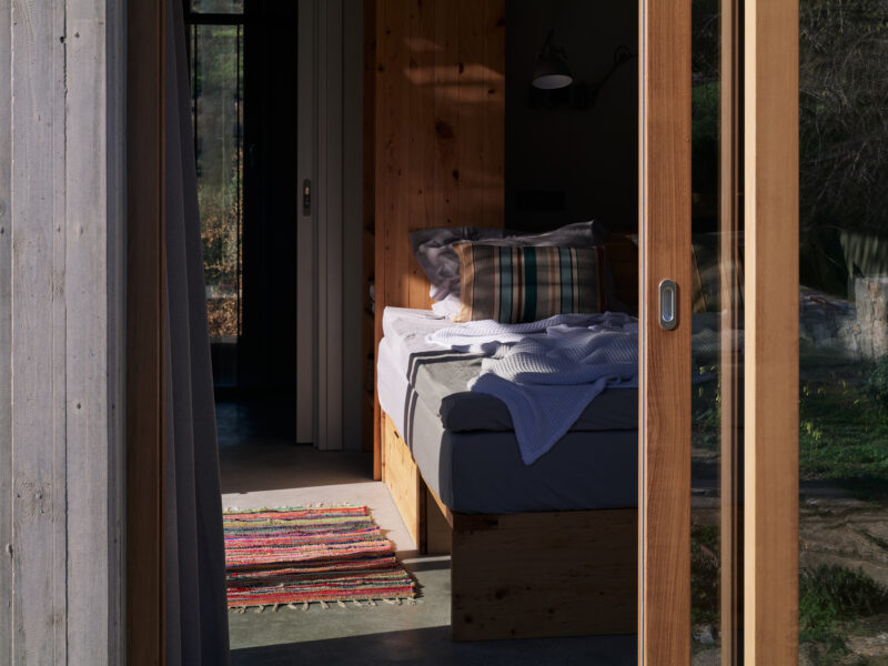 Cozy bedroom with natural light, featuring a bed with a striped pillow and a colorful rug in the foreground.