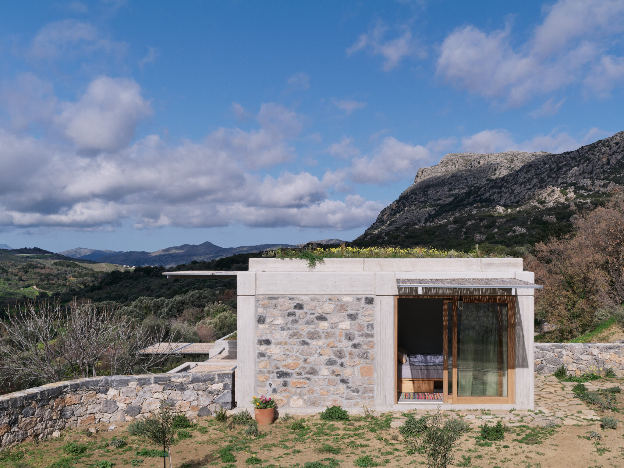 Exposed natural brickwork structure surrounded by greenery and mountains under a partly cloudy sky.