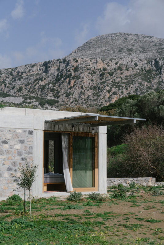 Modern stone building with a green curtain, set against a mountainous landscape and lush greenery.