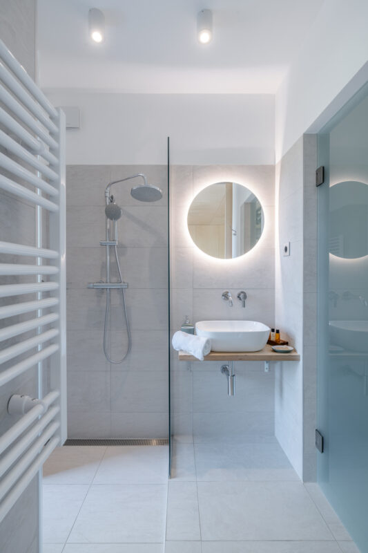 Modern bathroom featuring a shower with a rainfall showerhead, a round mirror, and a wooden sink countertop.