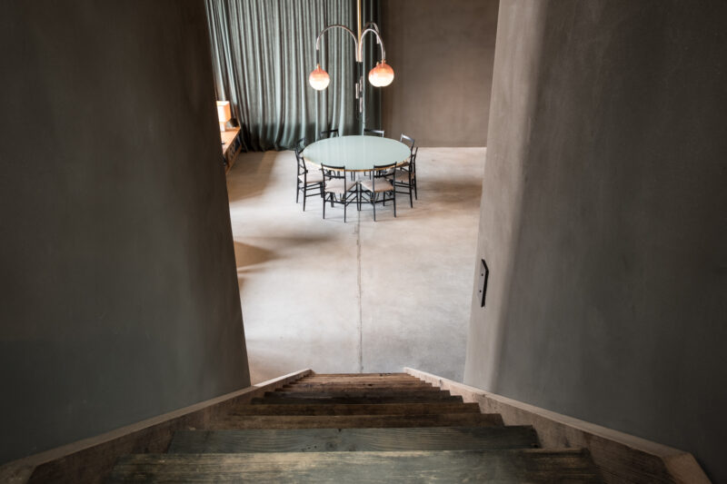 View from a staircase into a modern, minimalist room with a round table and pendant lights.