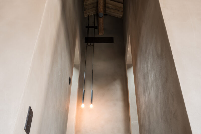 View from above of a narrow, minimalist stairwell with wooden beams and two pendant lights illuminating the space.