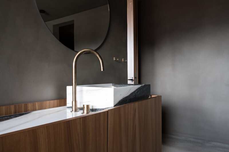 Modern bathroom featuring a sleek marble sink with a gold faucet, set against a dark wall and circular mirror.